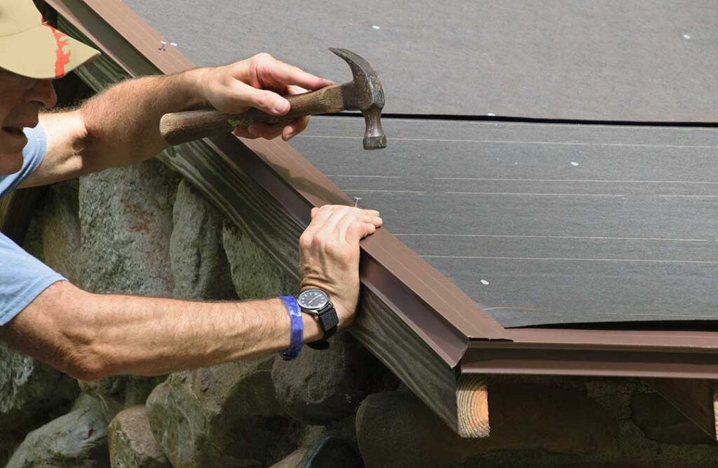 A close-up of hands gluing down the curled edge of an asphalt roofing shingle with roofing cement.