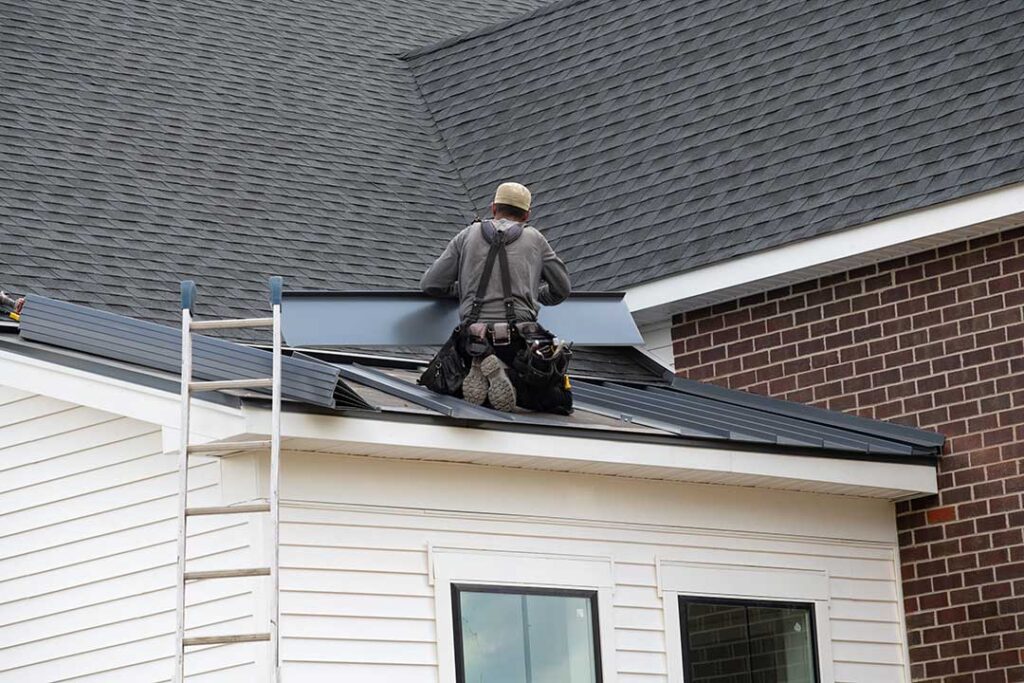 Homeowner inspecting gutters and roof edges beside a leaf-covered house in autumn