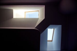 A sloped roof skylight with layered flashing, surrounding shingles, and light snow visible on the roof.