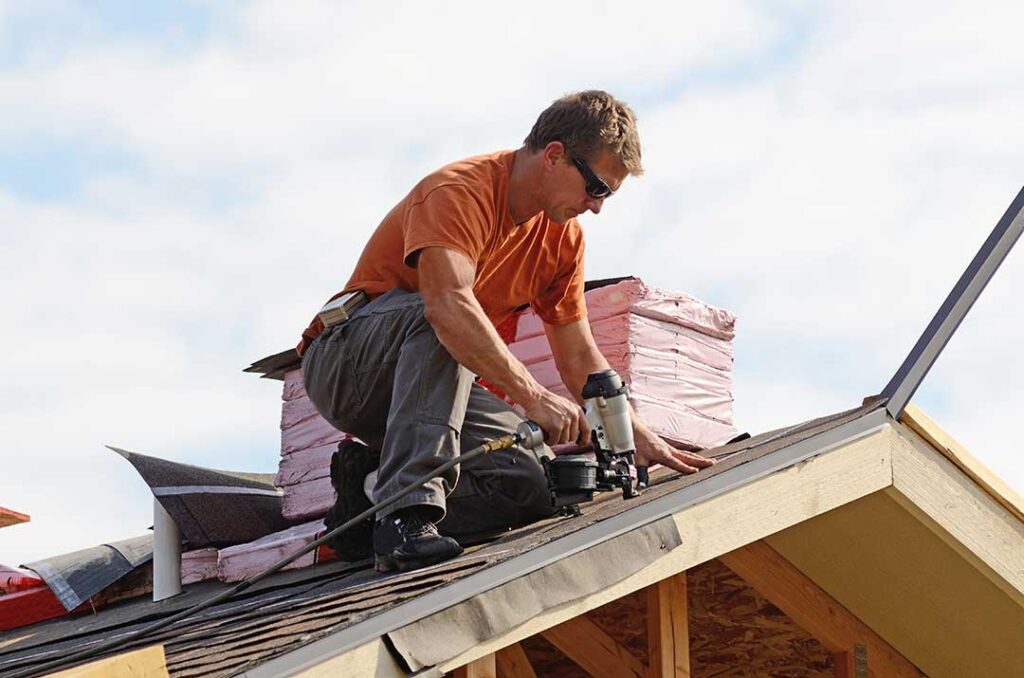 A homeowner examines a stained ceiling beneath a leaking roof while wet insulation is visible in the attic.